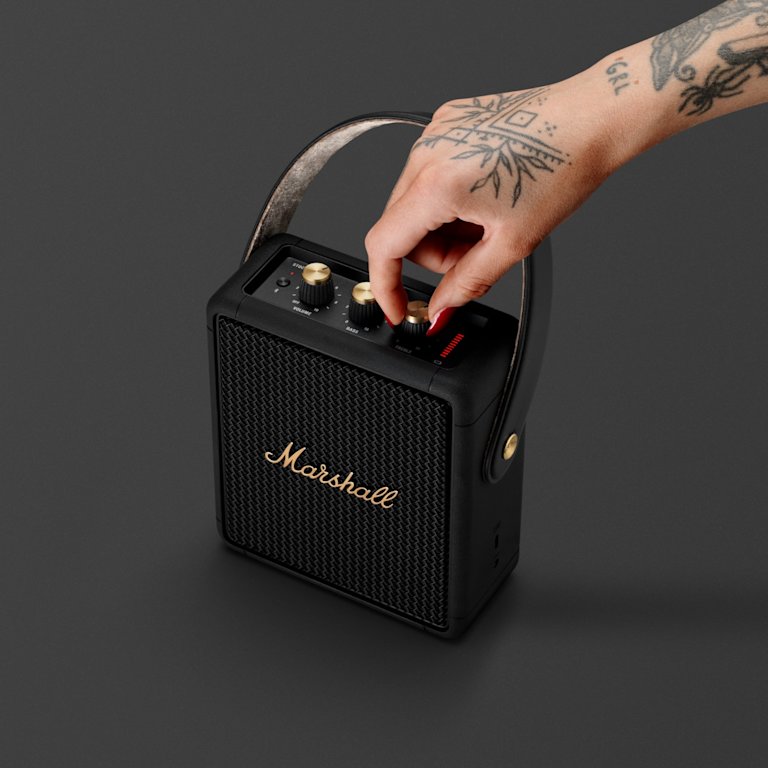 A person changing the volume of a Marshall Stockwell II Black and Brass portable speaker