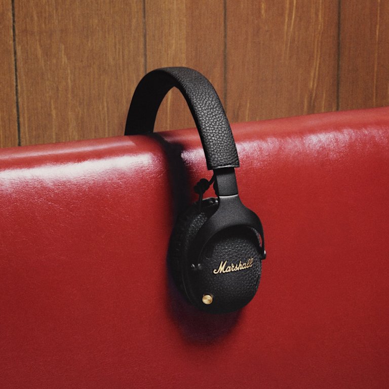 Marshall Monitor III A.N.C. Black over-ear headphones on the edge of a red bench against a wooden wall background.