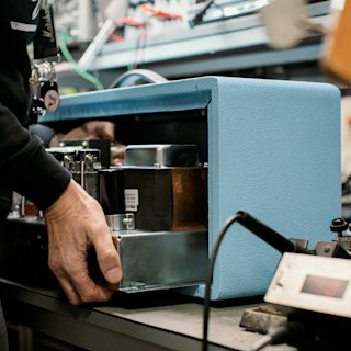 A person works on assembling 1959 BJA Artist Signature, at a workbench with tools and electronic components visible.