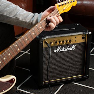 A person playing an electric guitar next to a Marshall amplifier on a black and white checkered floor.