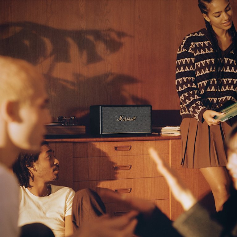 A group of people sitting in a room listening to music through a Marshall Stanmore III, a black Marshall speaker.
