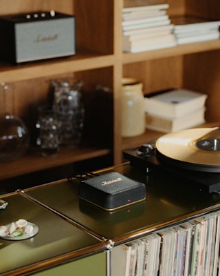 Heddon sits next to a vinyl record player, with shelves of books and glassware in the background.