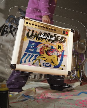 A person is carrying a Marshall Studio 900 Combo Lunar New Year Edition 2026 amplifier. Drums and paint splatters are visible in the background.