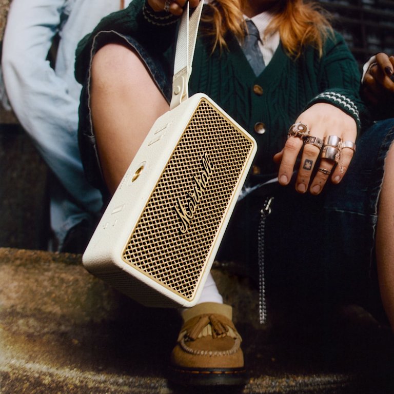 A person holds the Marshall Middleton II Cream portable Bluetooth speaker, with one foot on a step.