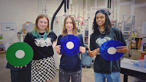 Three people smiling as they hold vinyl records.