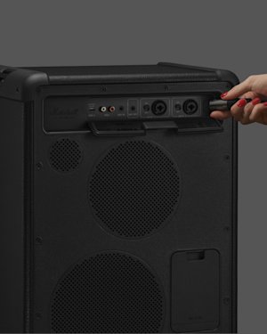 A person plugs a cable into the input panel of a black Marshall Bromley 450 against a plain gray background.