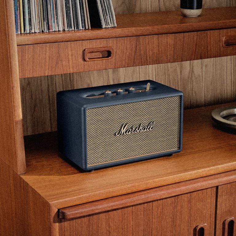 Marshall Acton III Midnight Blue Bluetooth speaker sits on a wooden shelf beneath a stack of records.