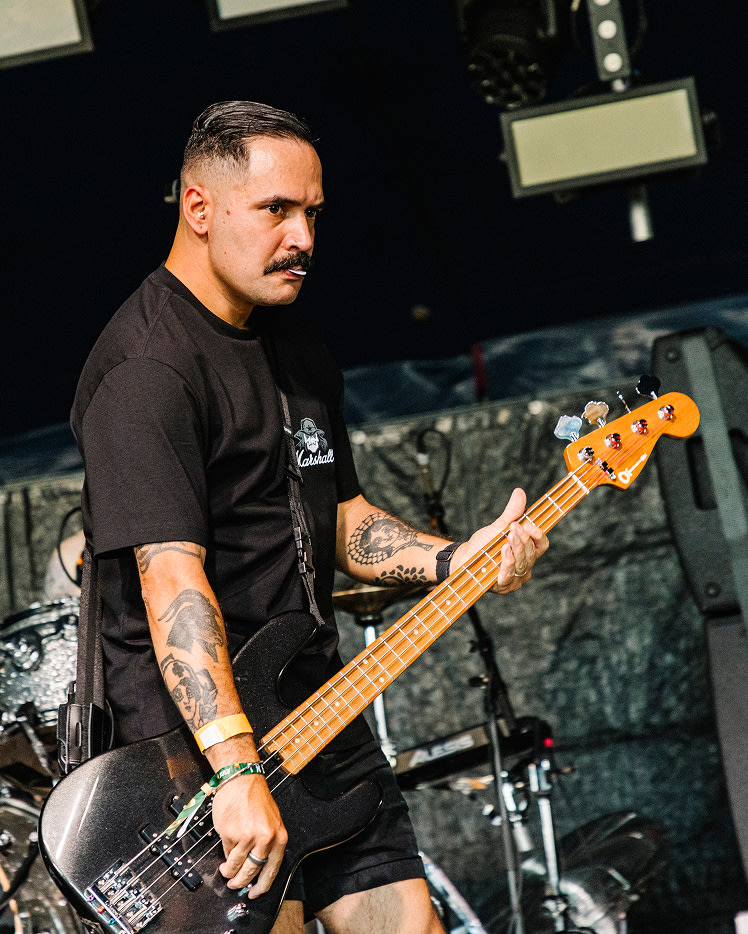 A musician playing a black electric bass guitar on stage and wearing Marshall Stax Reissue T-shirt.