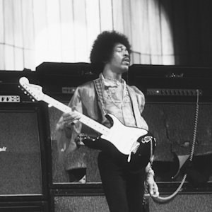 A black and white image of Jimi Hendrix holding his guitar in front of the Marshall Amplifiers