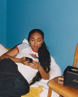 A girl in a Blue room looking at her phone whilst listening to music on Acton III