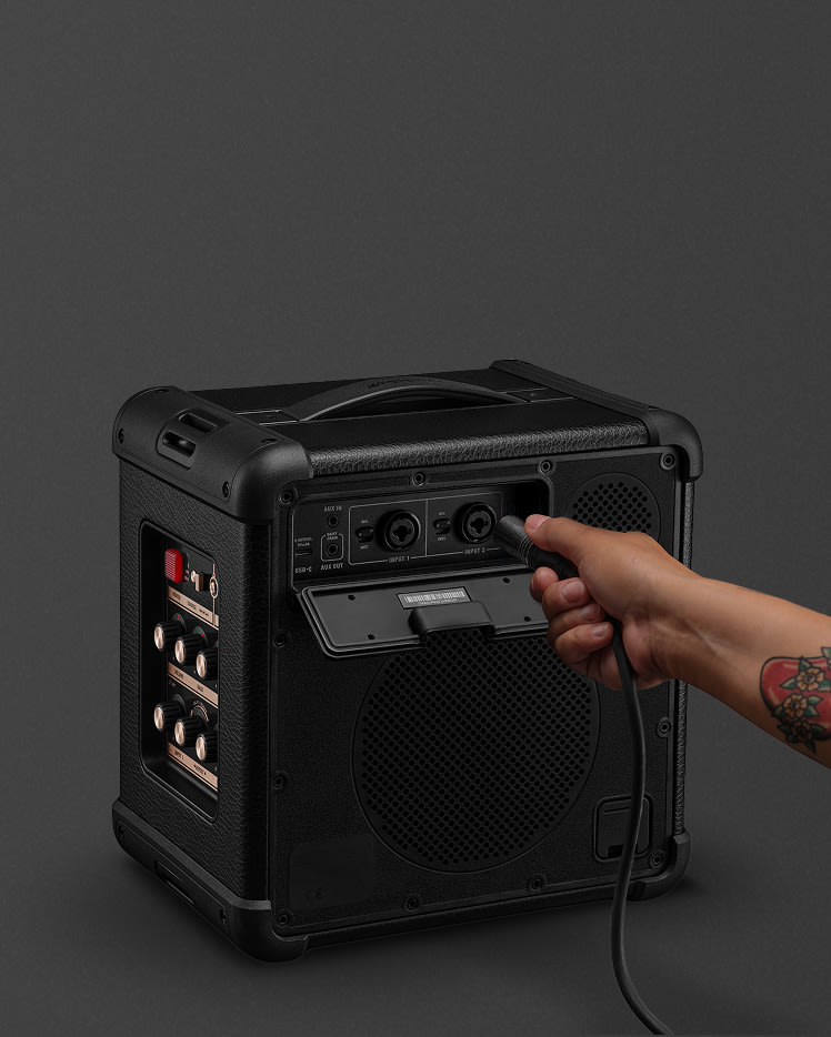 Plugging a cable into the Bromley 150 Black and Brass with control knobs and various input/output ports on its side.