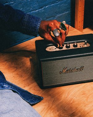 A person with several rings adjusts the controls on Acton IV Black speaker placed on a wooden surface.