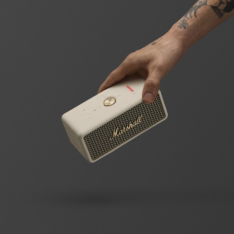 A hand holding Marshall Emberton III Cream speaker against a dark background.