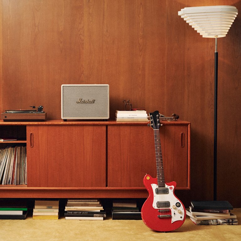A red guitar sitting in front of a Marshall Woburn III Cream.