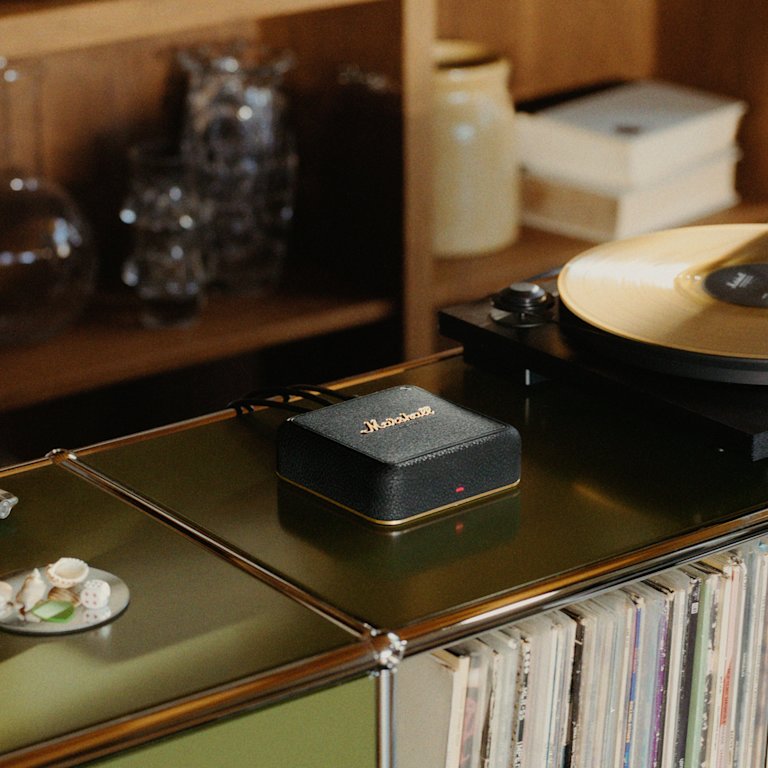 A record player with a yellow vinyl sits on a shelf next to Marshall Heddon, with books and glassware in the background.