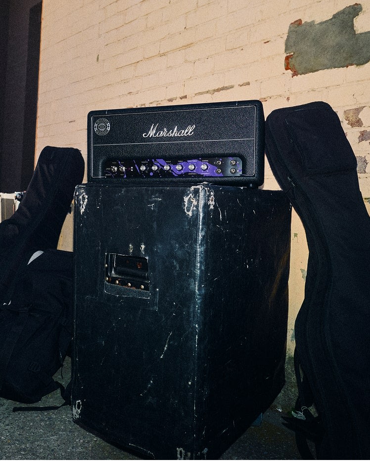JMH Studio Head sits on top of a worn black equipment case, with two guitar cases leaning against a brick wall in the background.