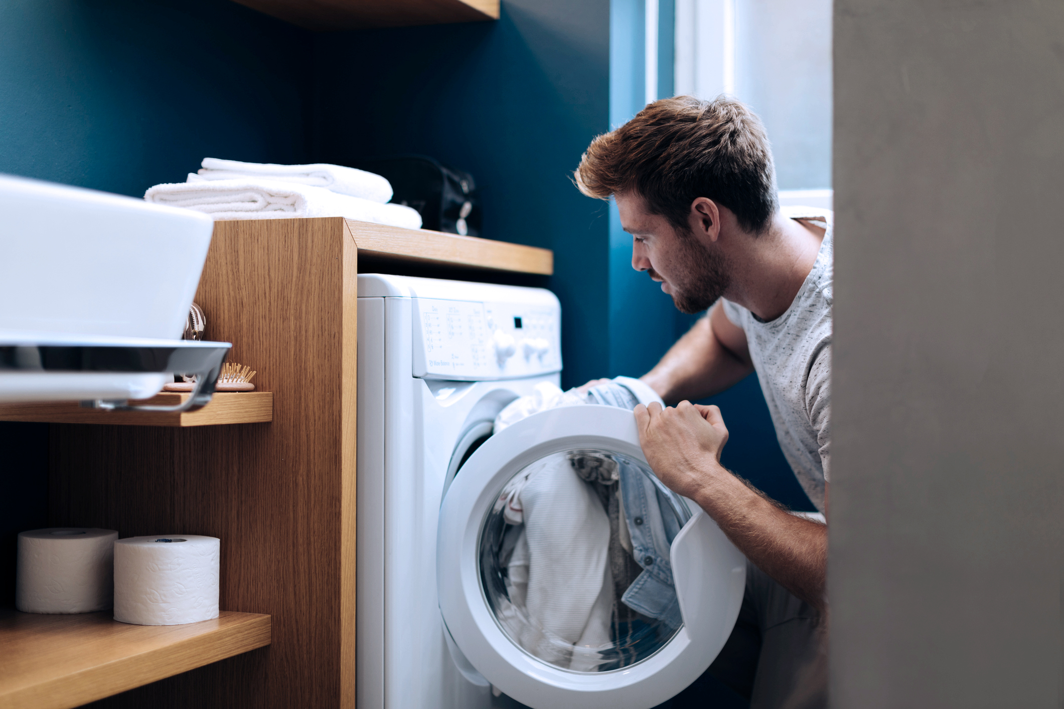 Mann som putter inn skittentøy i vaskemaskinen