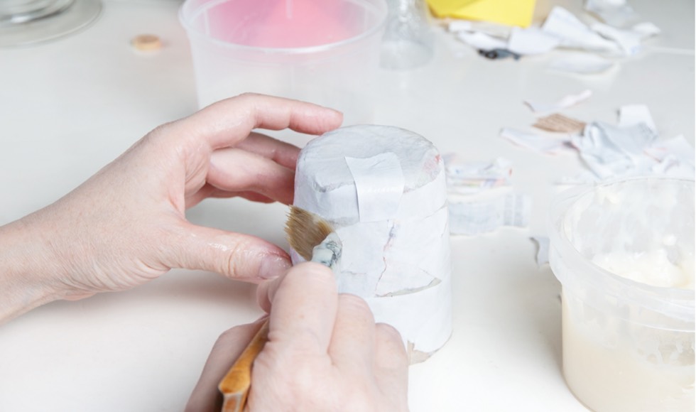Hand brushing glue onto paper strips to make a papier-mâché