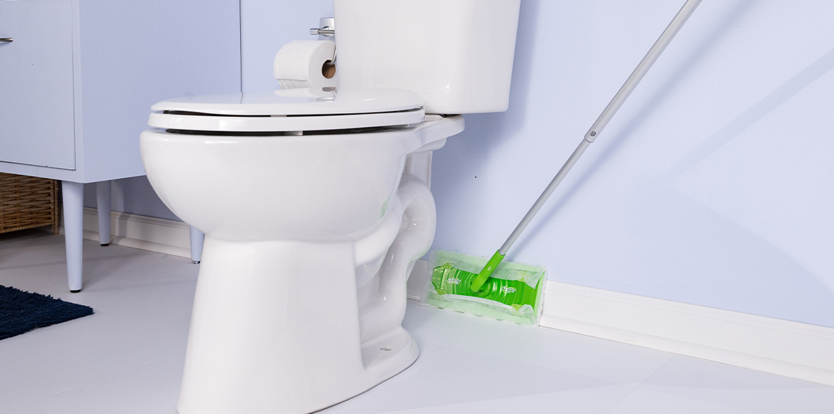 White toilet in a clean bathroom with a green floor mop leaning against the wall beside it.