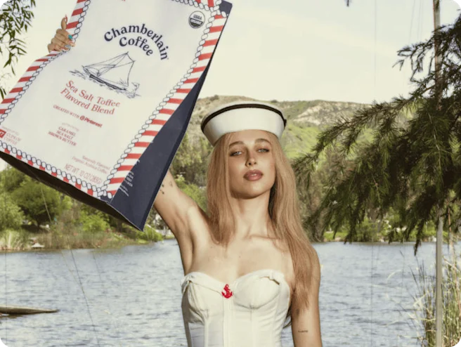 Image of Emma Chamberlain in a white sailor outfit holding a bag of Chamberlain Coffee