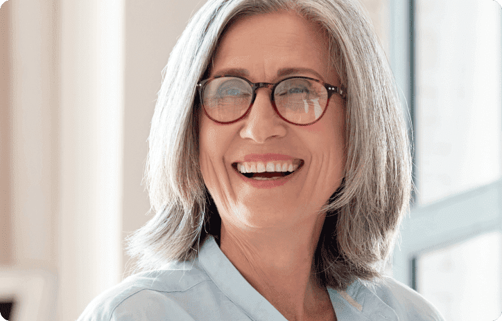 Older woman with shoulder length gray hair and glasses smiling
