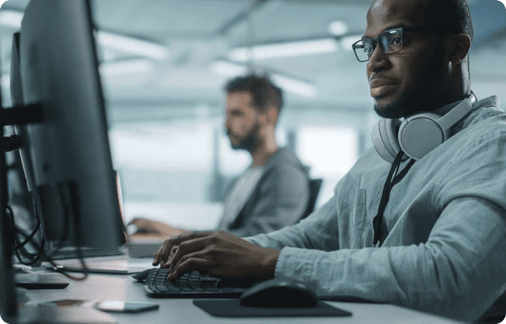 Man sitting at computer with glasses and headphones around his neck