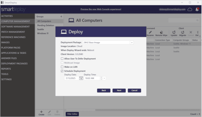 Screenshot of the SmartDeploy interface showing the "Deploy" dialog box in front of the "All Computers" view. The dialog contains deployment options including a dropdown to select the deployment package ("2482 Base Image") and displays the image location as "Cloud." It includes settings for reboot behavior, client version (3.0.2040), and checkboxes for "Allow User To Defer Deployment," "Wake on LAN," and "Schedule Deployment." Deployment is scheduled for 7/15/2025 at 10:02 AM. Buttons labeled "Back," "Next," and "Cancel" appear at the bottom. The underlying screen lists computer details such as name, model, and location.
