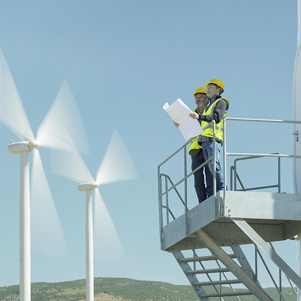 Workers standing on a metal platform with windmills in the background