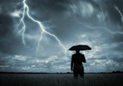 Man with umbrella looking at lightning storm.