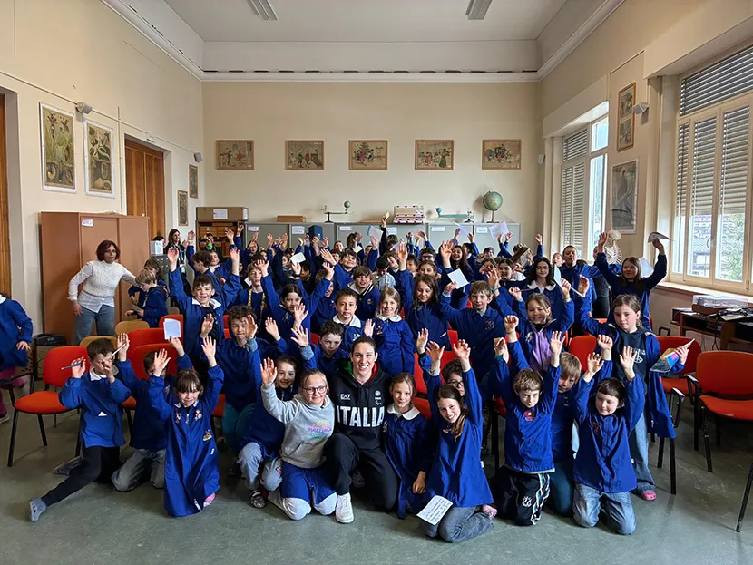 Un gruppo di circa 100 studenti tra i 6 e gli 8 anni posano in gruppo insieme a Carlotta Gilli all'interno di un'aula magna della loro scuola dopo aver seguito il racconto del programma educativo Campioni Ogni Giorno