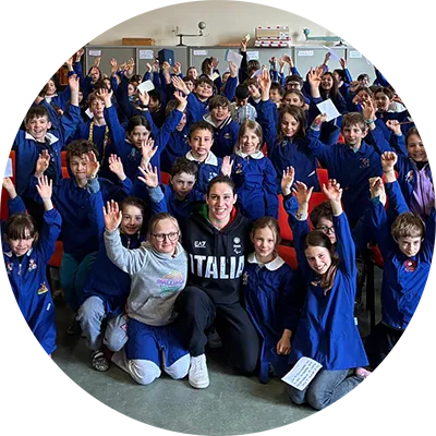 i bambini delle 5 classi della scuola elementare Duca D’aosta di Cortina D’Ampezzo posano in gruppo insieme a Carlotta Gilli all’interno di un’aula magna dell’istituto.