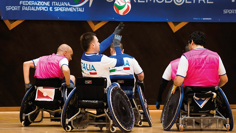 Cinque ragazzi della nazionale italiana in sedia a ruote giocano in una palestra a rugby nella sua versione paralimpica