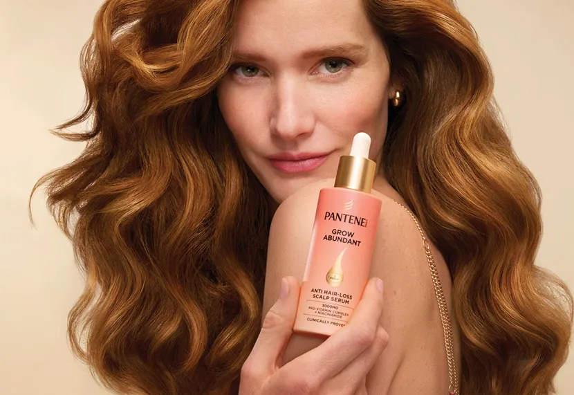 una donna con capelli castani tiene in mano un flacone di pantene grow abundant. I suoi capelli sono folti e lucenti.