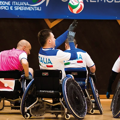 un gruppo di ragazzi in sedia a rotelle gioca all’interno di una palestra a rugby paralimpico.