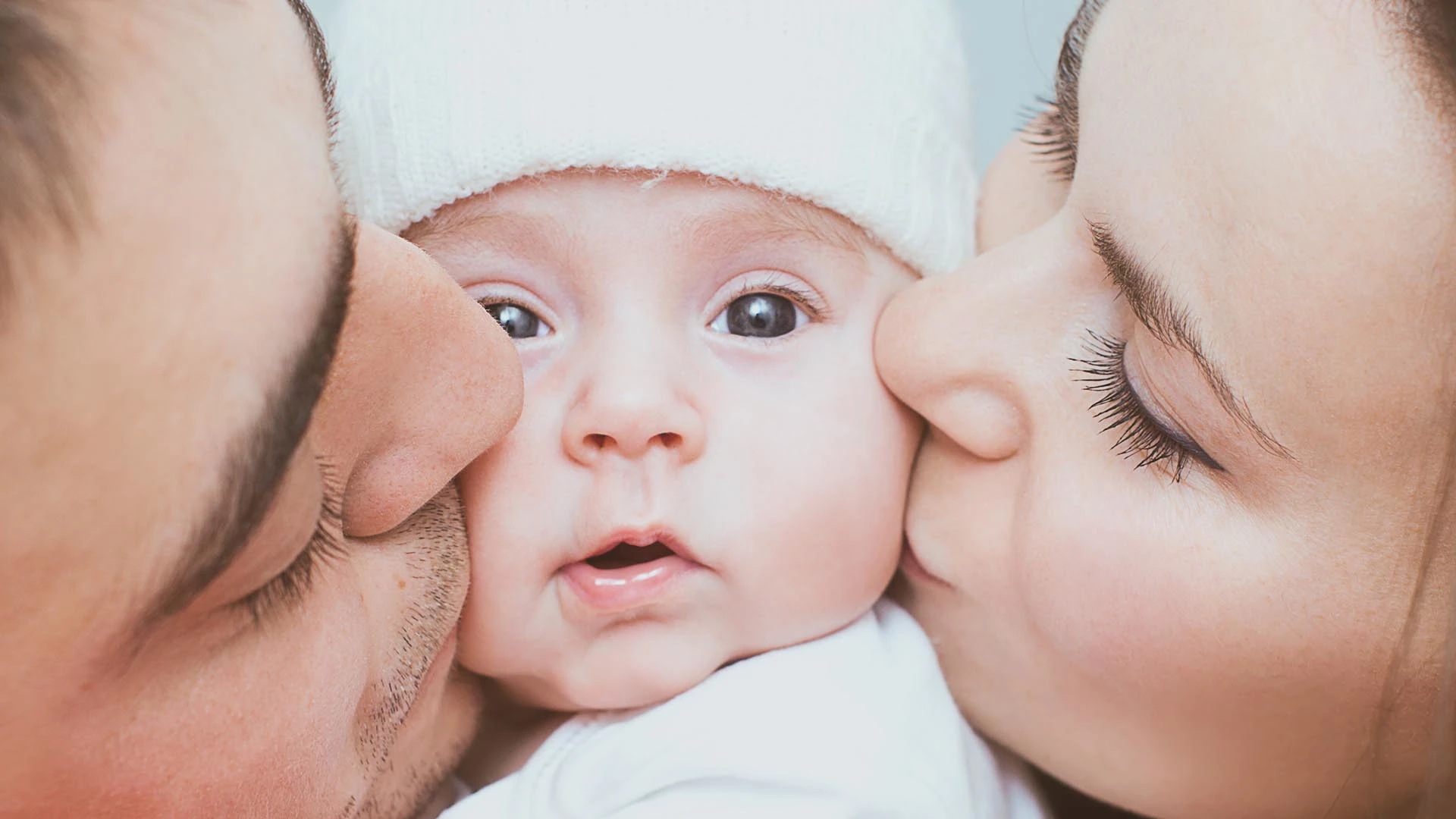 Una mamma e un papà che baciano sulle guance il figlio appena nato