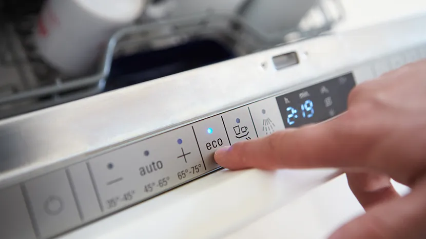 Una persona sceglie la modalità eco e i detersivi Fairy per la sua lavastoviglie, in modo da ridurre il consumo energetico a casa.
