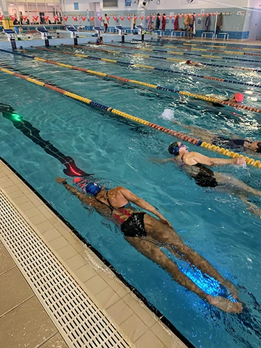 una nuotatrice in piscina nuota a stile libero, sotto di lei i led emanano impulsi luminosi per guidarla.