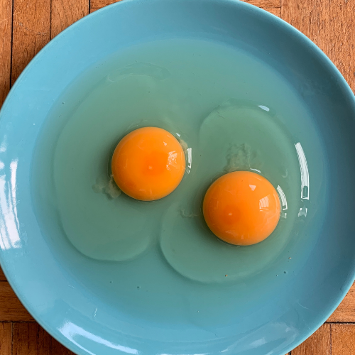 Świeże jajka wbite na talerz z przylegającym, gęstym białkiem