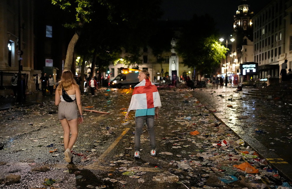 Two England supporters walk past litter on a street in central London, Sunday, July 11, 2021, after Italy won the Euro 2020 soccer championship final match between England and Italy played at Wembley Stadium. (AP Photo/Matt Dunham)