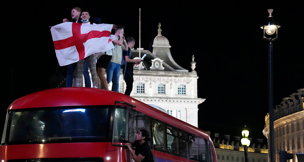 Fans celebrate on top of a bus in central London after England won the Euro 2020 soccer championship semifinal match between England and Denmark played at Wembley Stadium, London, Wednesday, July 7, 2021. (AP Photo/Thanassis Stavrakis)
