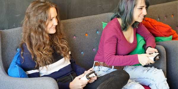 两个年轻的女人坐在沙发上玩电子游戏，看着屏幕，手里拿着游戏机控制器，玩得很开心
