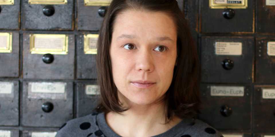portrait of katrin friedmann standing in the clue office in front of wooden drawers of a lock