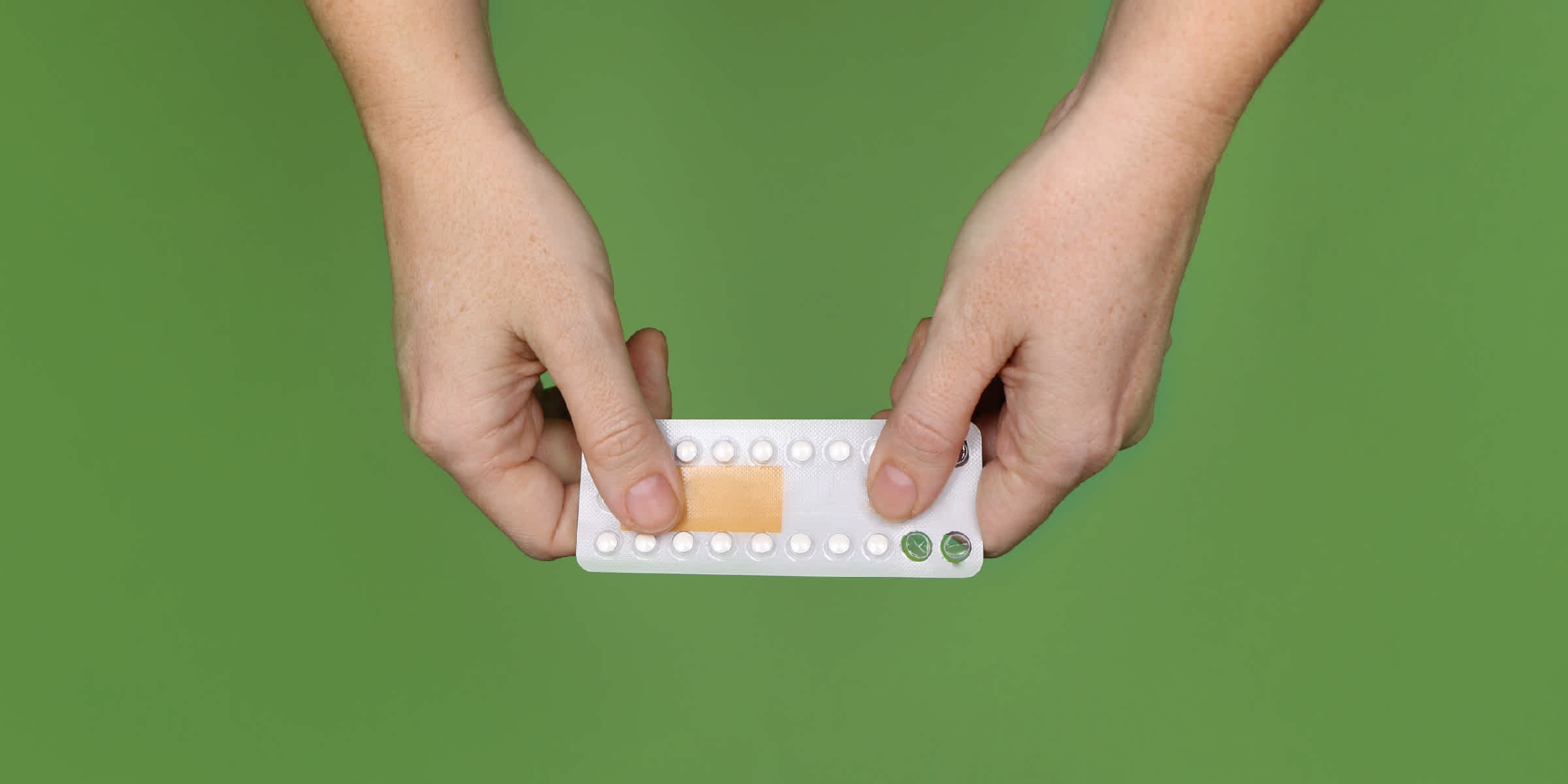 Two hands holding a sheet of birth control pills