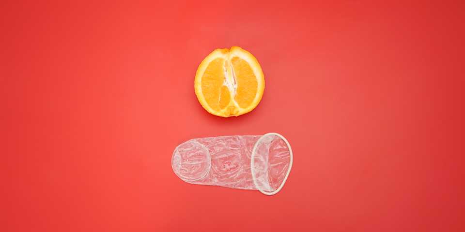 Um preservativo feminino desempacotado, mostrado ao lado de uma laranja para uma perspectiva do tamanho.