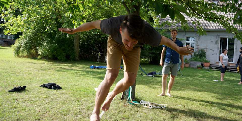 a man walking from tree to tree on a slackline in the summer