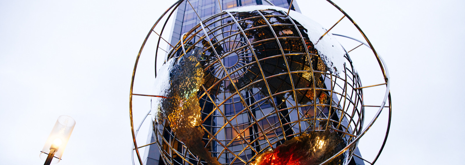 Image looking a spherical globe sculpture in front of a sky scraper