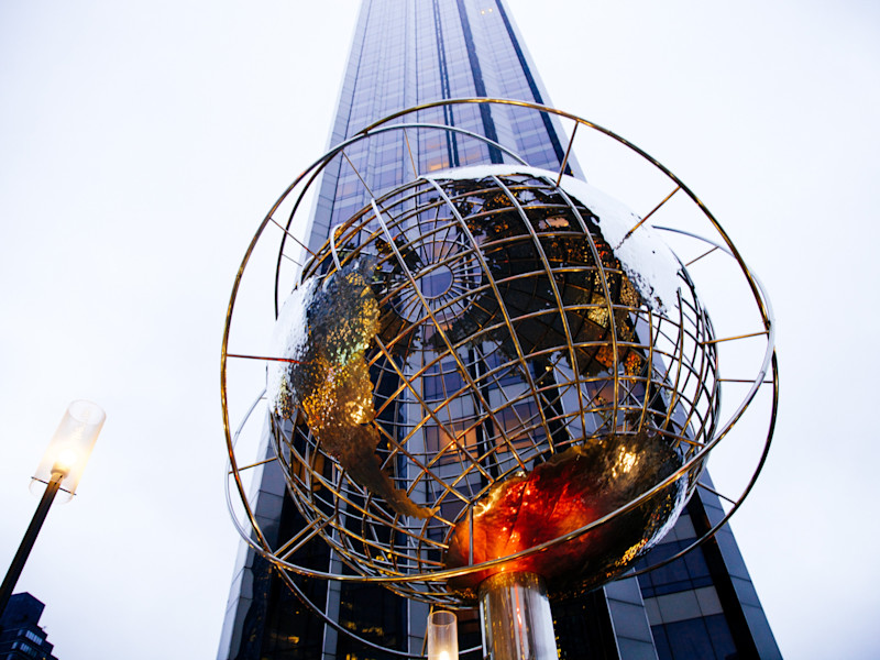 Image looking a spherical globe sculpture in front of a sky scraper