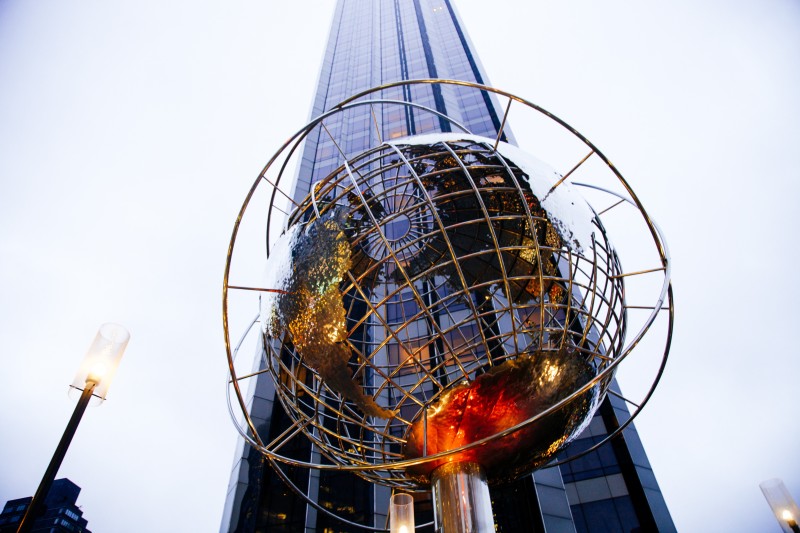 Image looking a spherical globe sculpture in front of a sky scraper