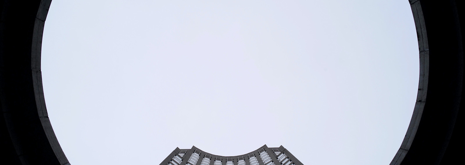 Image looking up towards a tall corporate tower through a circular building
