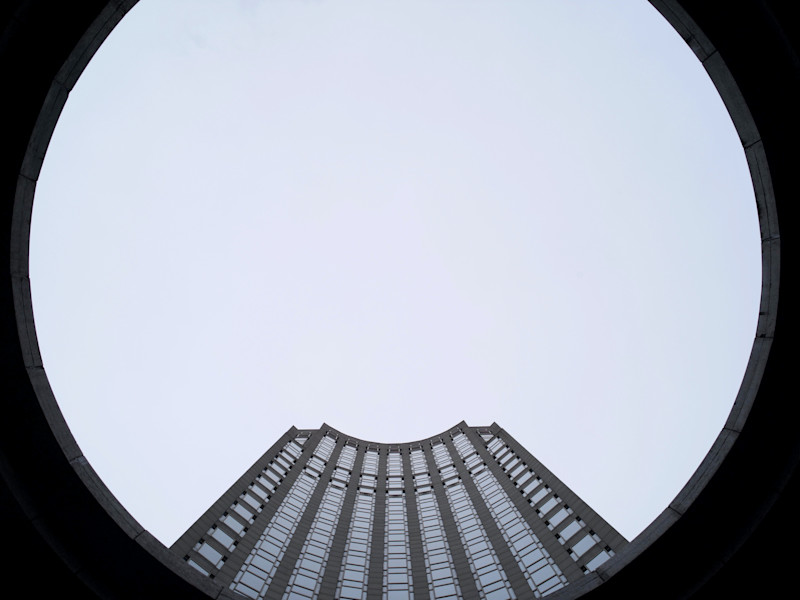 Image looking up towards a tall corporate tower through a circular building